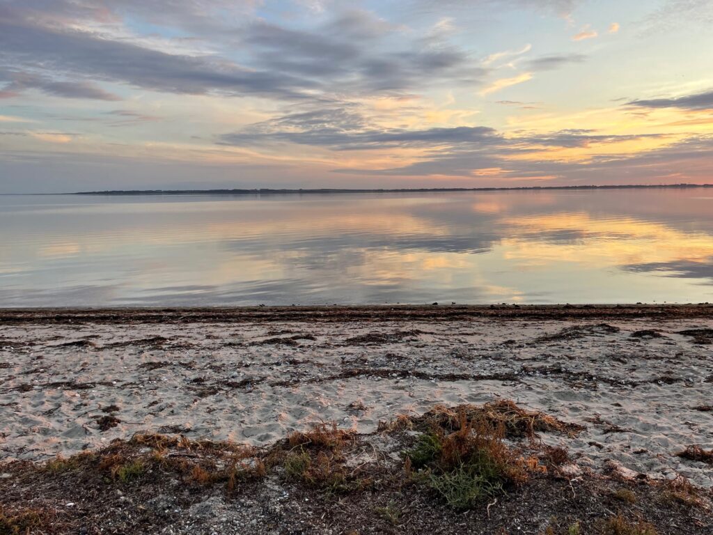 Aftenstemning ved strand med solnedgang over vandet