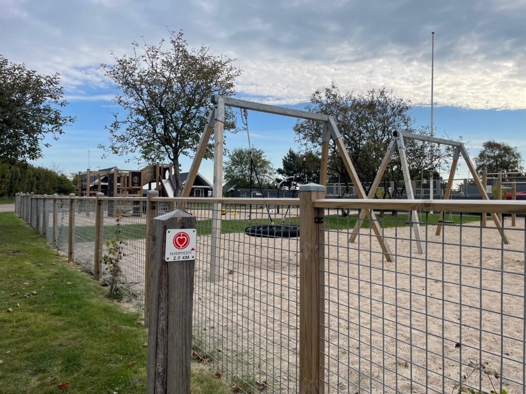 Indhegnet legeplads med gynger og rutsjebane